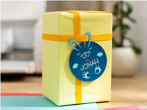 Woman's hands using transfer tape to adhere the blue vinyl onto a small drinking glass