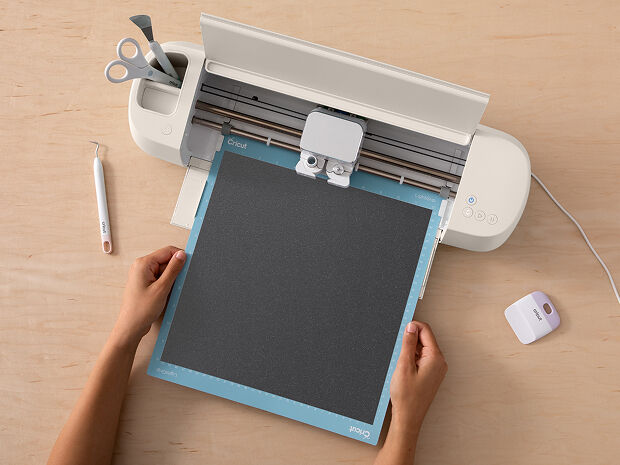Woman's hands using transfer tape to adhere the blue vinyl onto a small drinking glass
